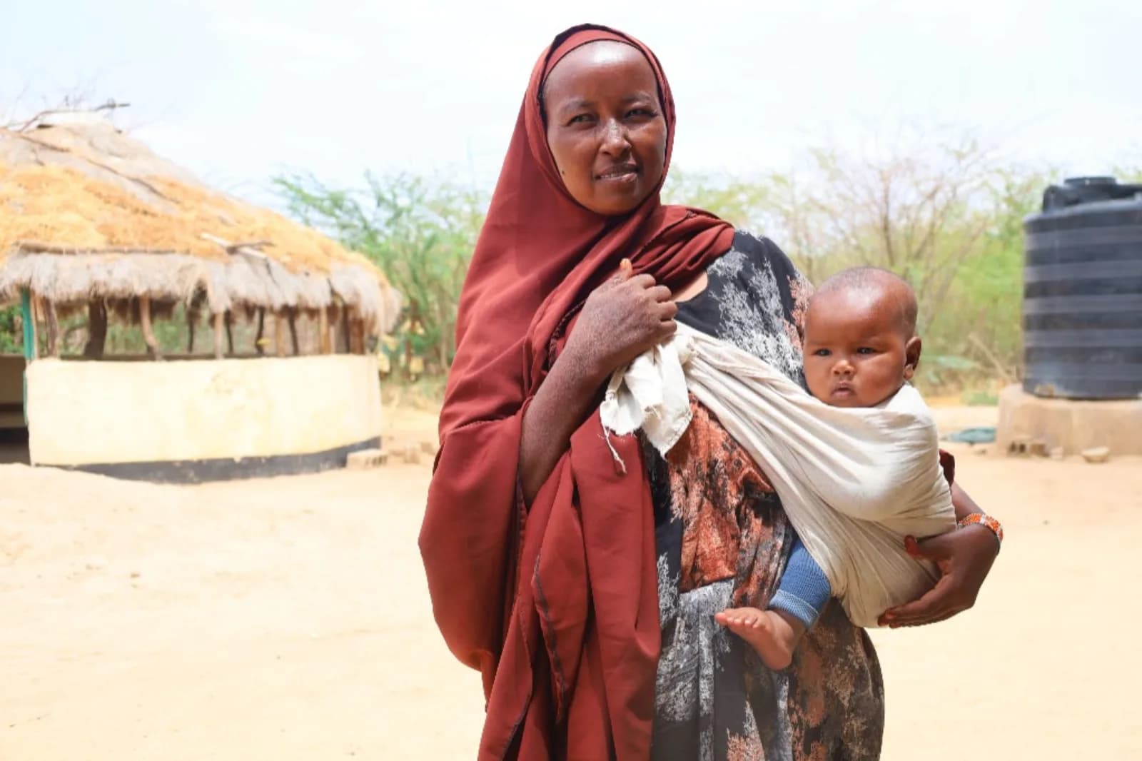 A mother carrying her baby outside her homestead.